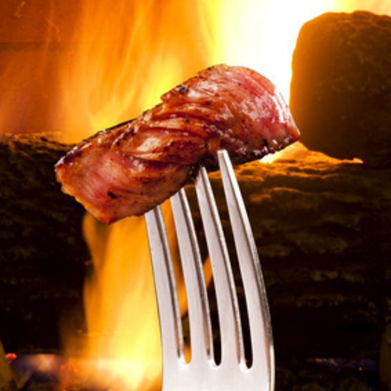 Slice of cooked rib eye filet held on a fork over the grill